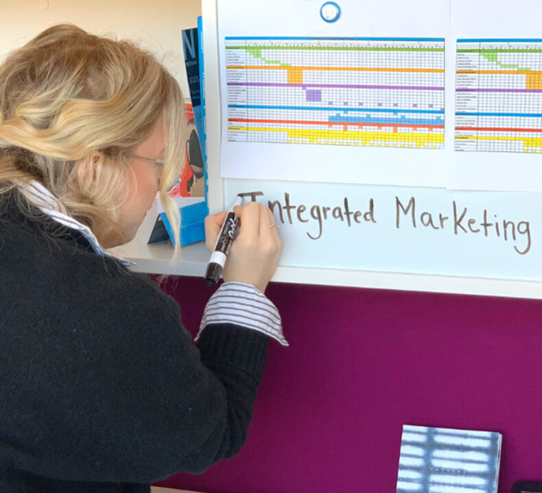 A woman writing on a white board the words Integrated Marketing
